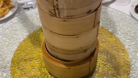 close-up of hands placing dim sum into bamboo steamers on a dining table.