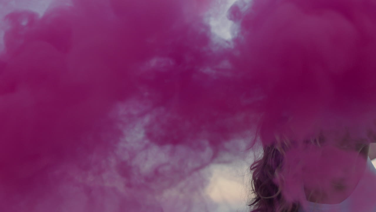 hermosa mujer agitando granada de humo rosa bailando en la playa temprano en la mañana celebrando la libertad creativa