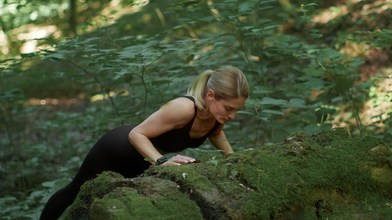 Woman doing push-ups on a mossy log in a forest