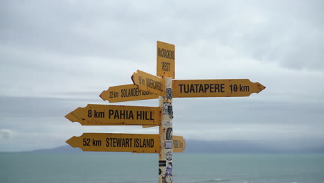 A-yellow-sign-stands-against-the-backdrop-of-the-sea-at-McCracken's-Rest,-South-Island,-New-Zealand