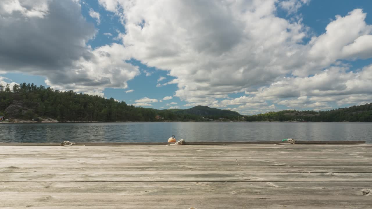 Time lapse of clouds forming over countryside lake, wooden pier dock