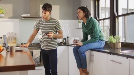 feliz pareja de hombres diversos bebiendo café y usando computadora portátil en la cocina
