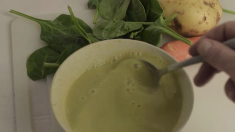 hand stirring healthy vegetable soup in a bowl with vegetables in background close up