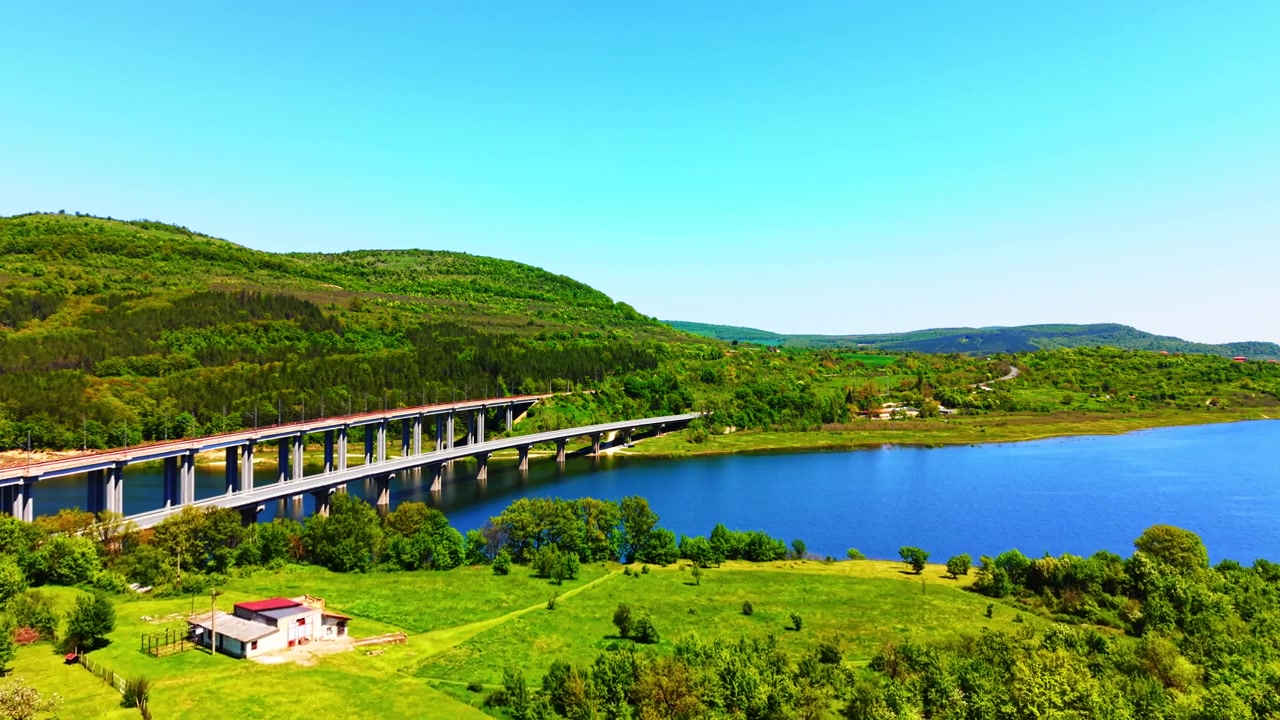 保加利亞水庫上的鐵路橋。高角度拍攝現代混凝土高架橋橫跨藍色水面，周圍環繞著生機勃勃的草地景觀