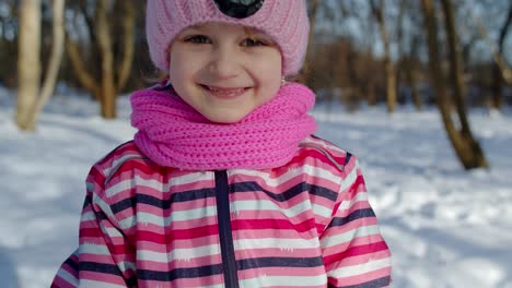 Child-girl-running-on-snowy-road,-fooling-around,-smiling,-looking-at-camera-in-winter-park-forest