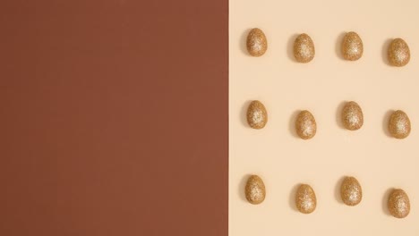 easter pattern with moving golden glitter eggs on nude brown background. stop motion flat lay