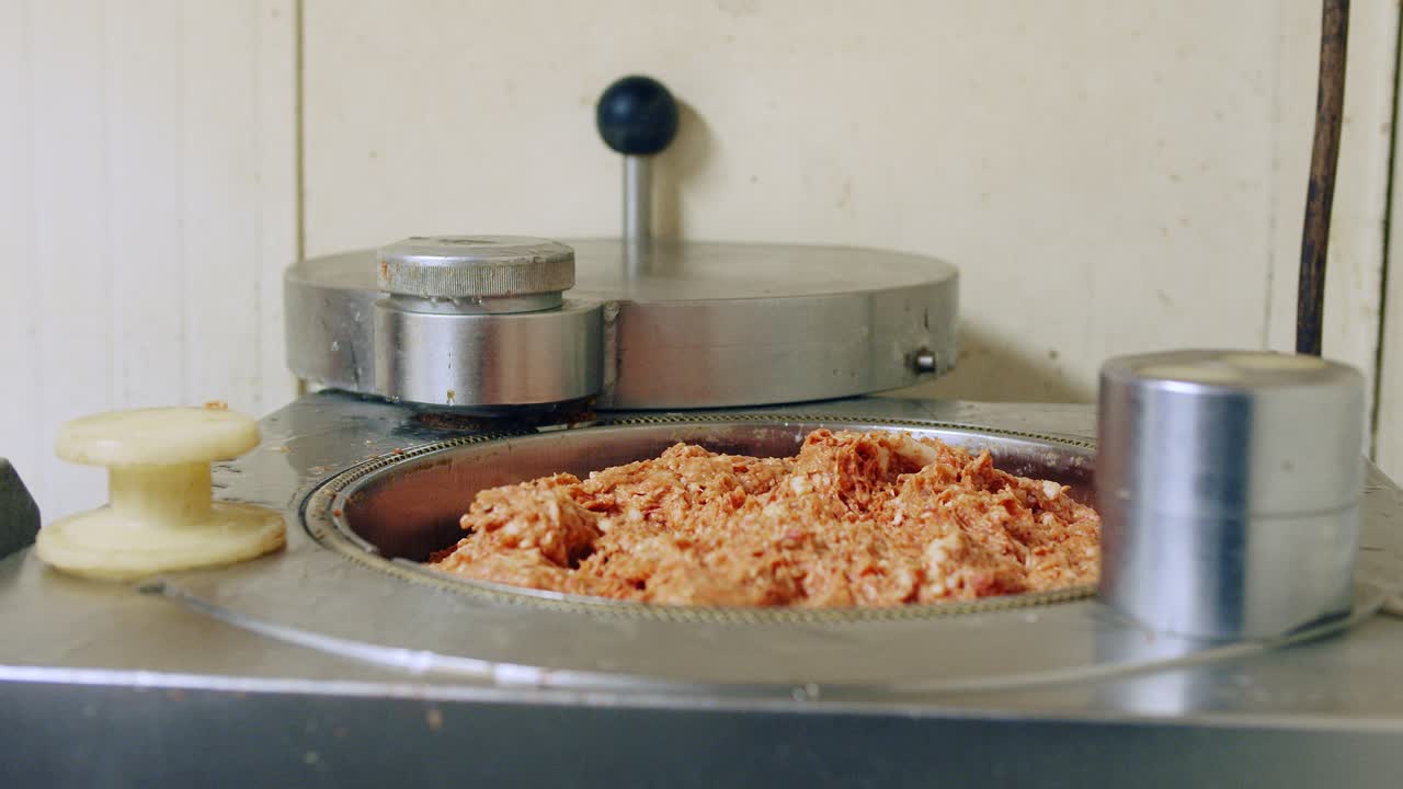 el carnicero llena el relleno de salchichas de la picadora eléctrica con carne cruda