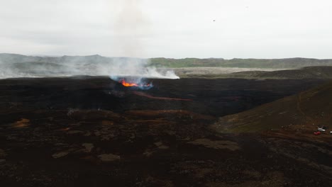 Aerial-landscape-view-over-people-looking-at-the-volcano-erupting-at-Litli-Hrutur,-Iceland,-with-lava-and-smoke-coming-out