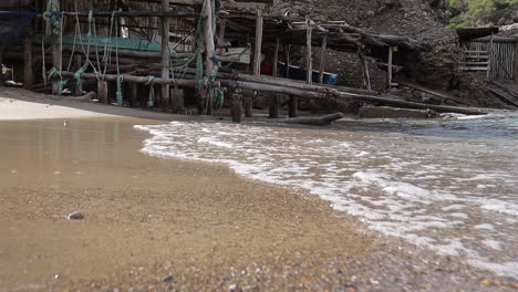 Low-slow-motion-shot-of-waves-splashing-on-a-tropical-beach-in-front-of-an-old-wooden-boat-house