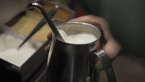 cafe worker turning off the steam frothing machine after preparing milk for a cappuccino