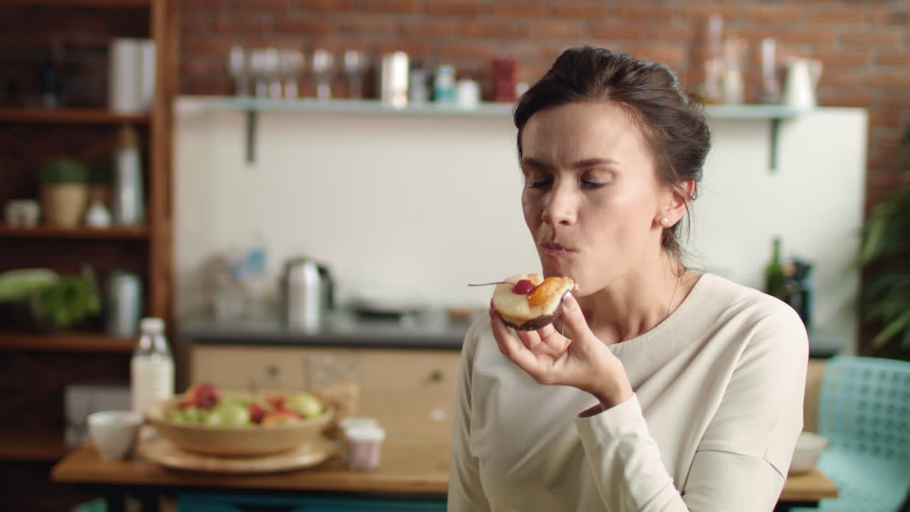 mujer mirando a la cámara con un pastel de lujo en la mano. chica mordiendo postre en casa.