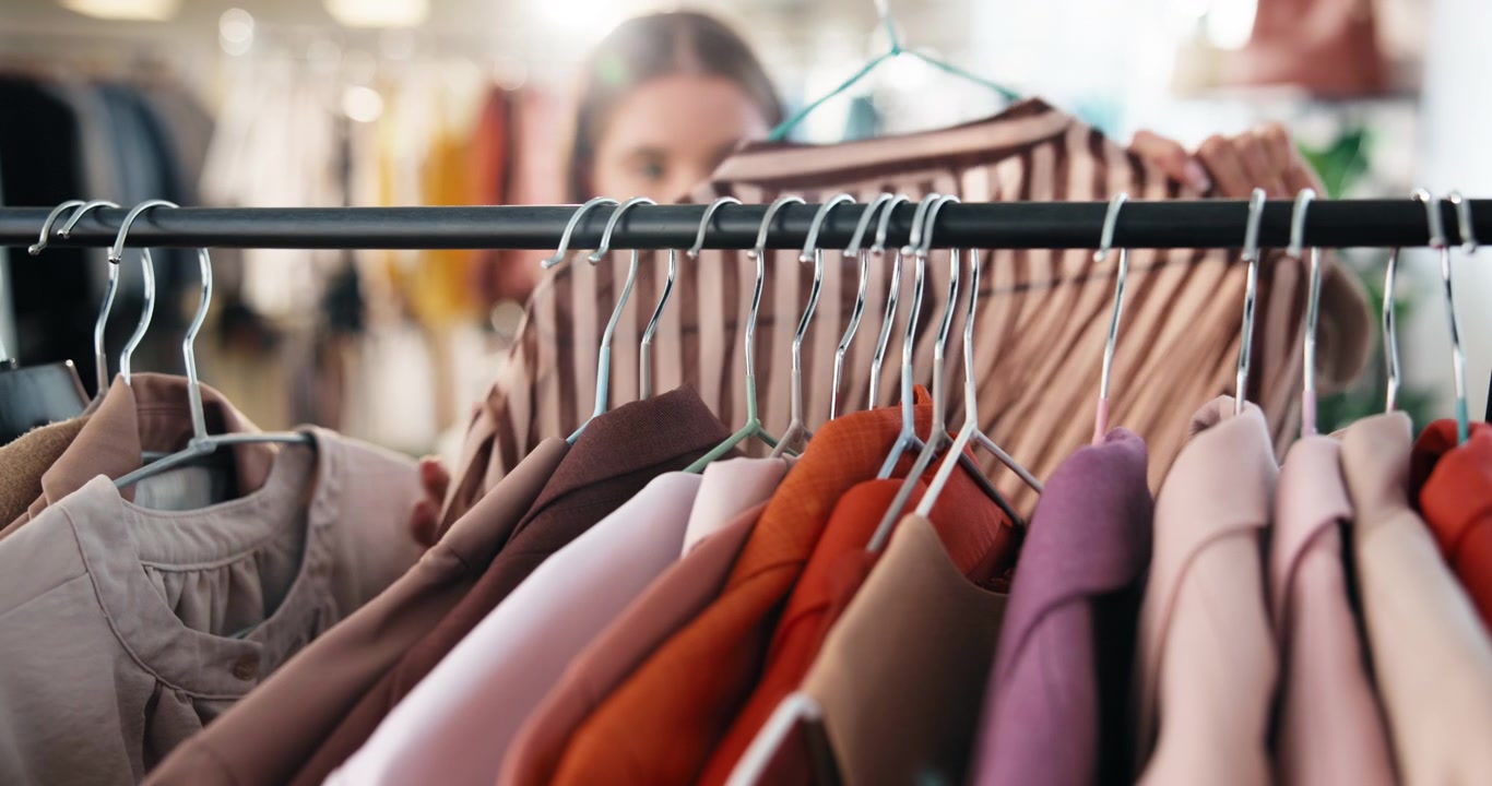 Giovane donna che guarda i vestiti su un appendiabiti in boutique