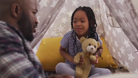 Happy-african-american-father-and-daughter-sitting-in-tent-and-telling-fairy-tales