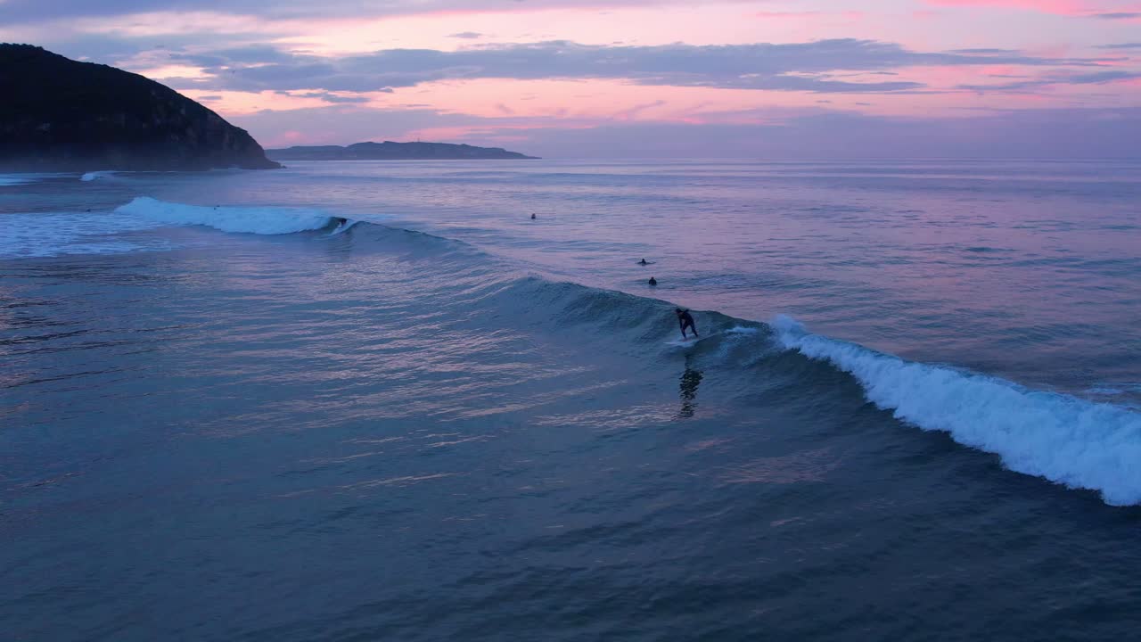 tiro de un dron de un surfista de un surfista atrapando una ola en la playa de berria en cantábrico, españa al atardecer