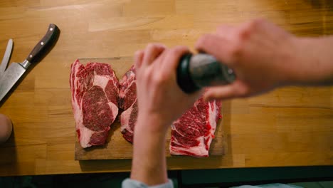 top view of man grinding black peppercorn on red delicious steak meat preparing for cooking