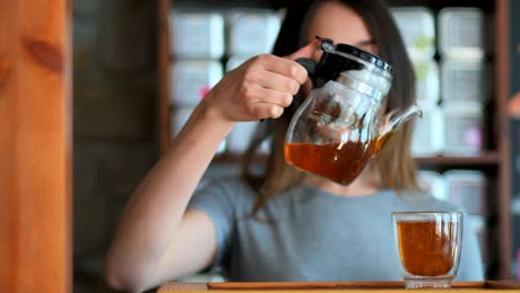 young smiling woman pouring red tea from glass kettle to smal cup