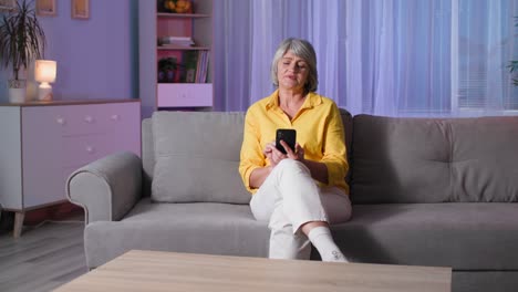 technologies for the elderly, gray-haired woman holding a mobile phone with green screen, modern grandmother uses a gadget at home while sitting on the couch