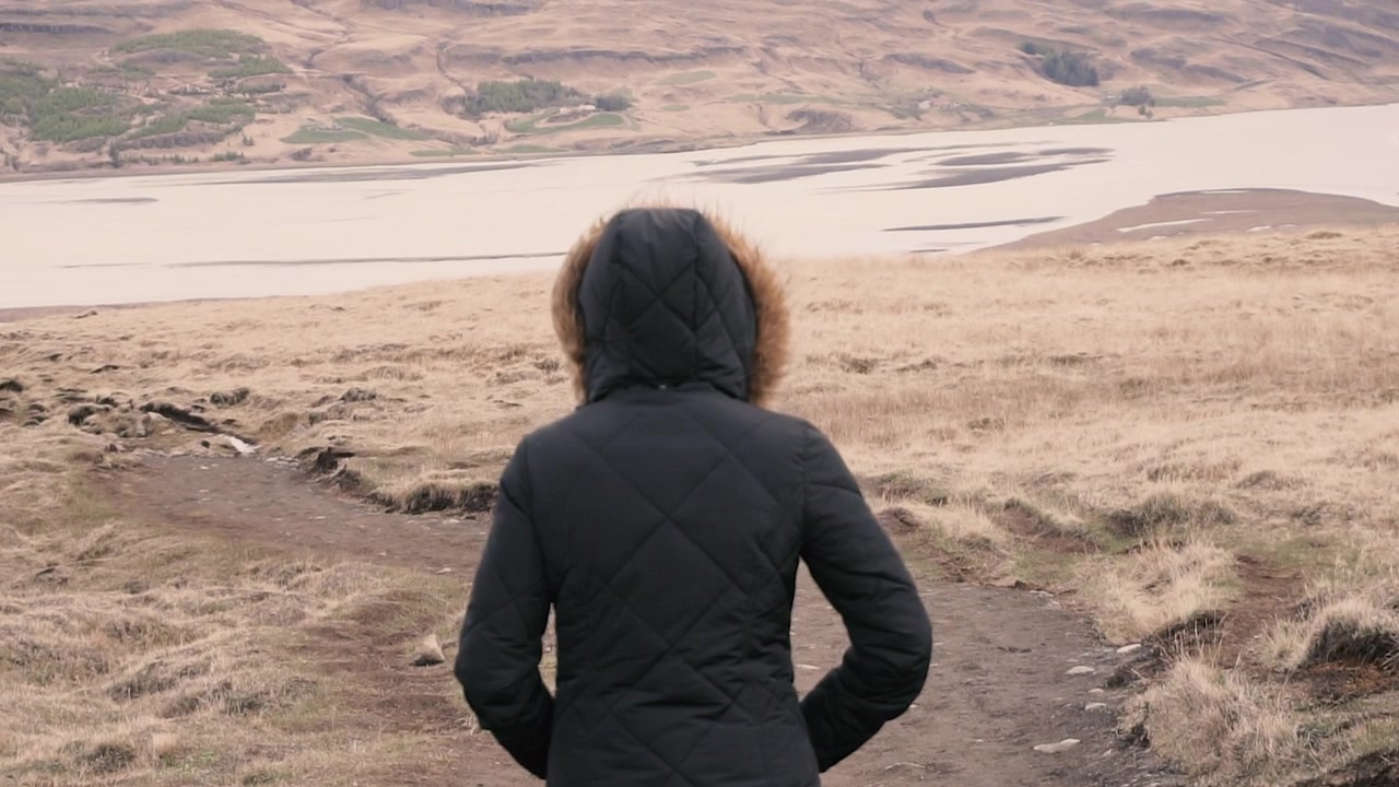 Woman in Winter Coat Walking on a Dirt Path in a Dry Landscape