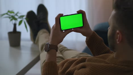 adult man is looking on display of modern smartphone with green screen technology relaxing and viewing video at break time in office or home