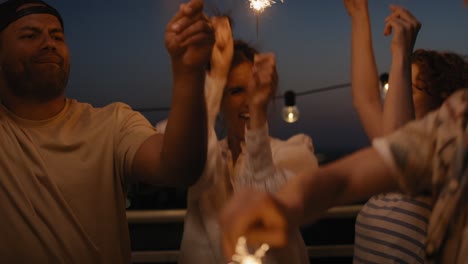 friends celebrating together at the rooftop with sparkles at night.