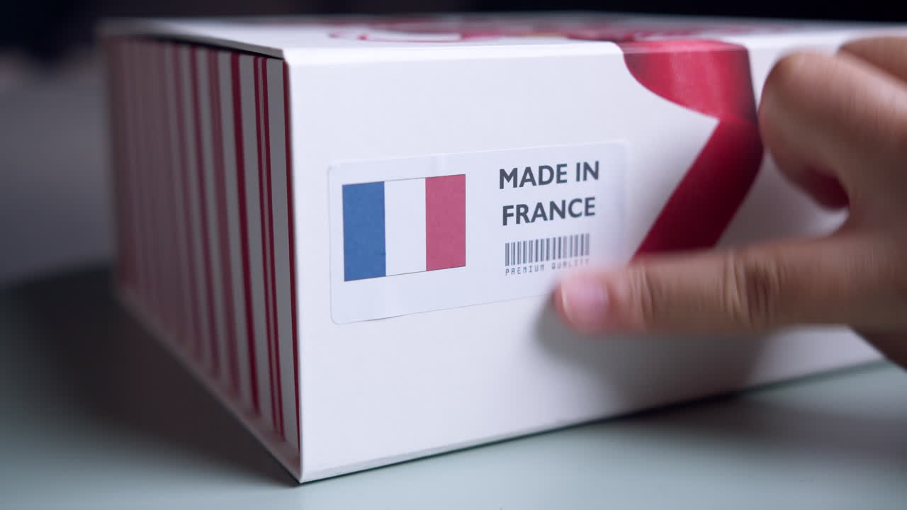 Mani che applicano l'etichetta con bandiera MADE IN FRANCE su una scatola di cartone da spedizione con prodotti.