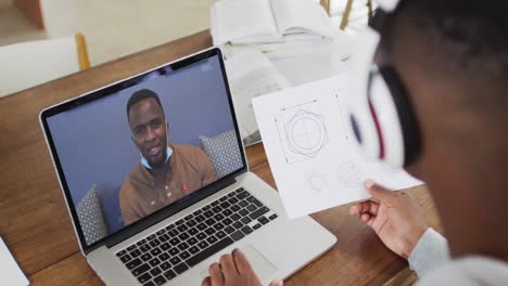 estudiante universitario afroamericano que sostiene notas mientras hace una videollamada en una computadora portátil en casa