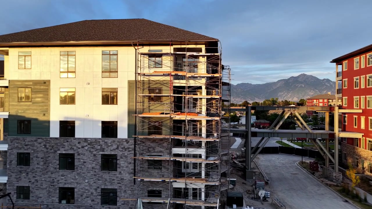Progetto di costruzione di appartamenti con edifici residenziali, ponteggi attivi, passerella pedonale sopraelevata e macchinari pesanti a Taylorsville, Contea di Salt Lake, Utah, Stati Uniti, ripresa con drone in avvicinamento.