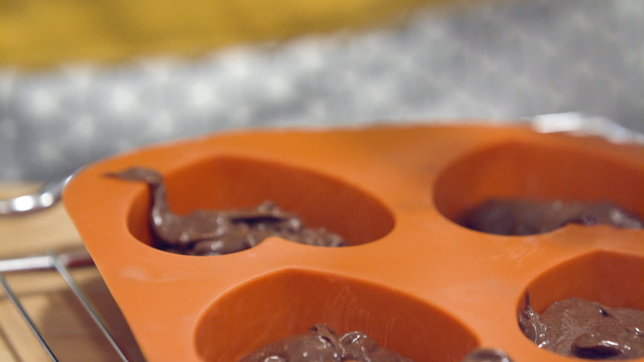 masa de chocolate goteando desde la cuchara hasta el molde naranja en forma de corazón - primer plano