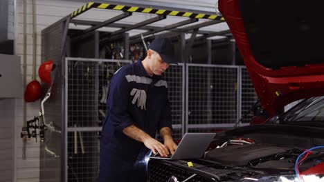 auto mechanic uses a laptop while conducting diagnostics test on engine