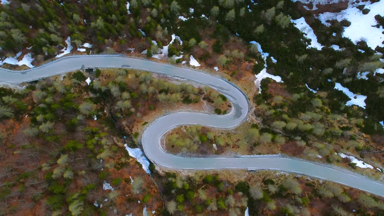 vista aérea de un dron volando por encima de la curva de la carretera forestal cerca de los picos de las montañas alpinas en primavera. manchas de nieve. imágenes de video con video de stock de drones