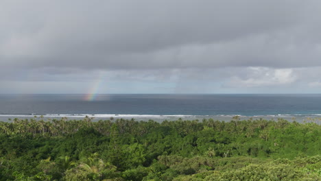 toma panorámica sobre la costa tropical con un arco iris cayendo al mar frente a la isla maré, nueva caledonia