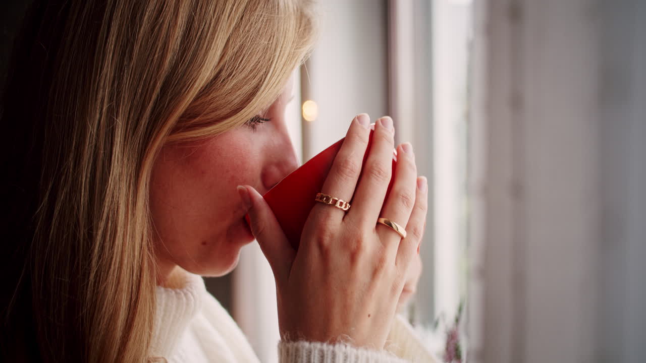 beautiful young blonde woman enjoying a mug of tea at the window