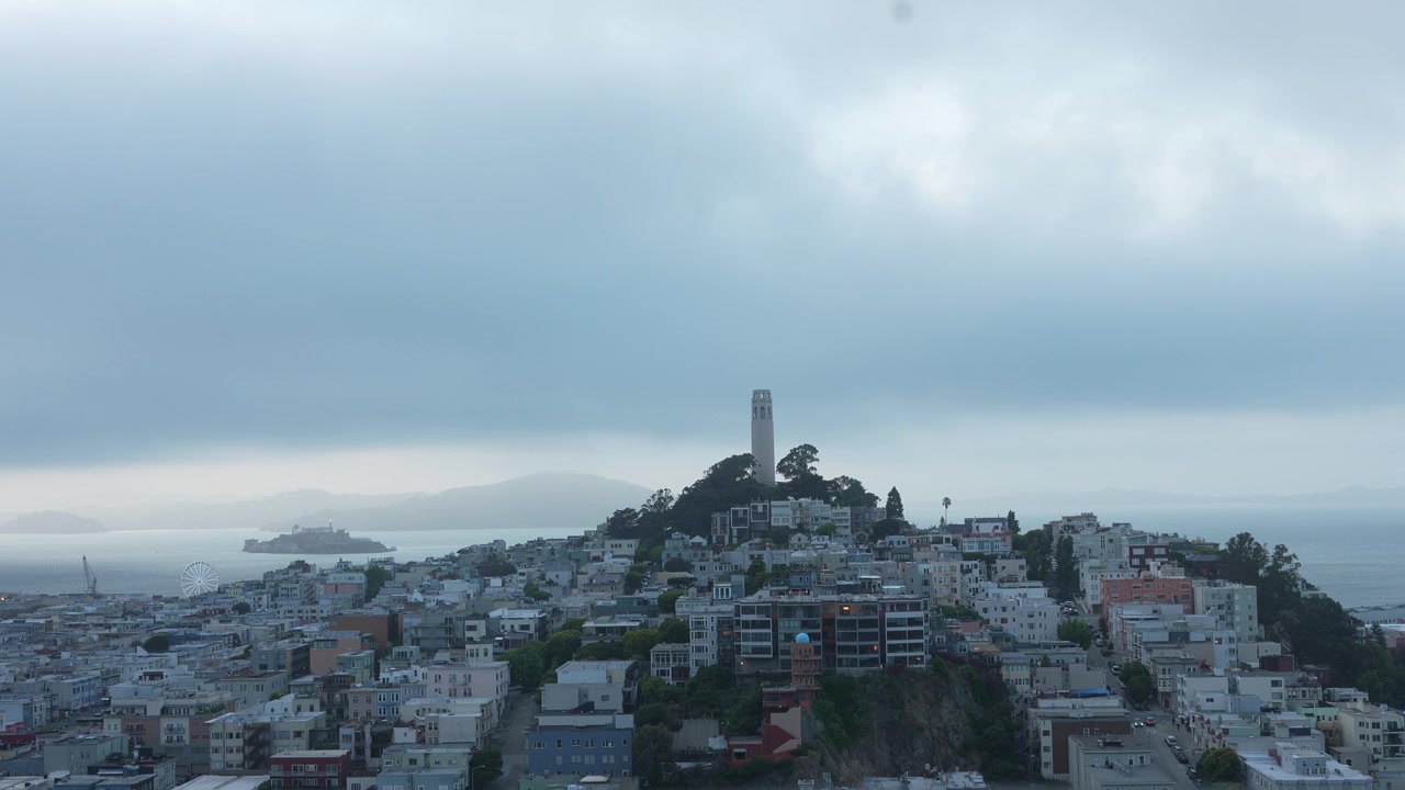 Cielo serale coperto con fitta nebbia che si estende sul paesaggio urbano di San Francisco, con la Coit Tower su Telegraph Hill, North Beach e l'isola di Alcatraz nella baia durante un tramonto suggestivo