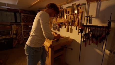 dolly in of a young man sanding the edge of a wooden plank in slow motion in a home workshop