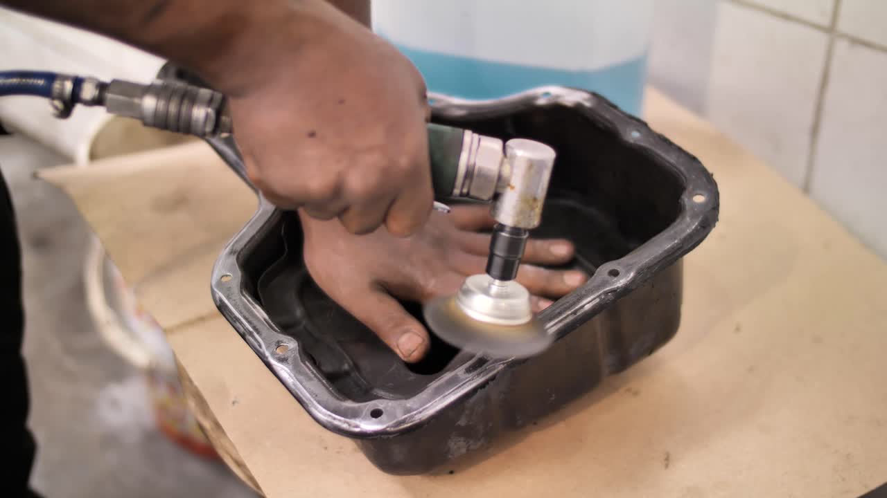 mecánico retira la junta del cárter de aceite del coche utilizando un cepillo de alambre en un dispositivo giratorio