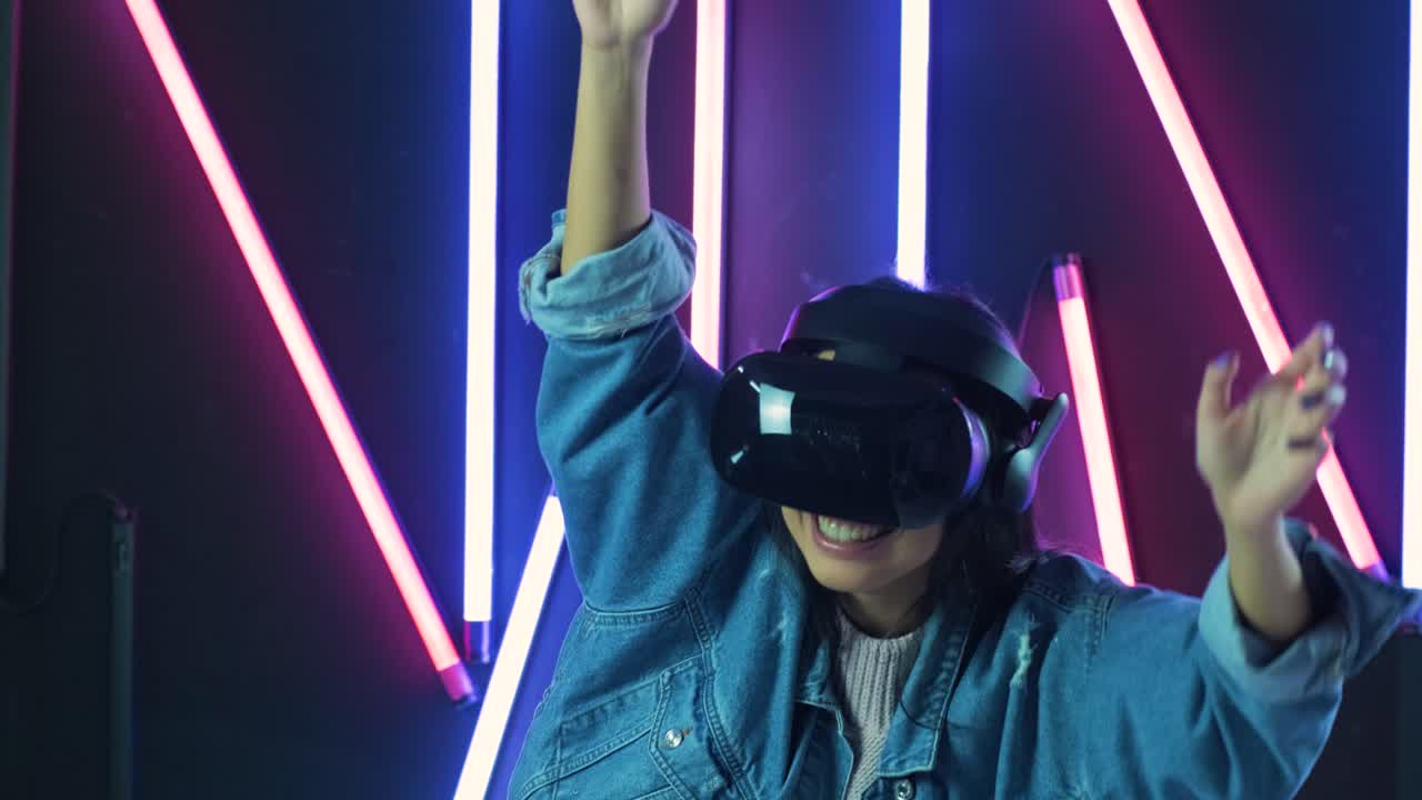 Giovane donna che balla e mani alzate con il visore VR. Casco per la realtà virtuale su sfondo con illuminazione colorata.