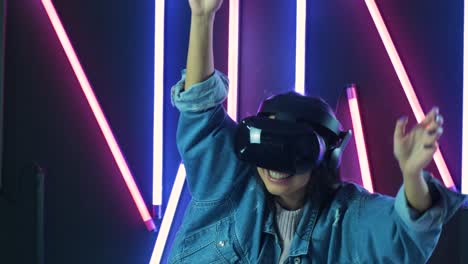 joven bailando y levantando las manos en el auricular vr. casco de realidad virtual en fondo de iluminación de color
