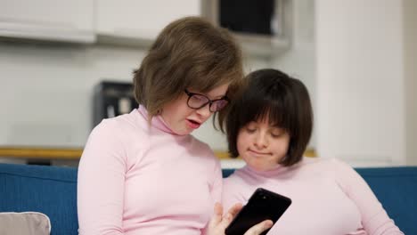 Two-girls-with-down-syndrome-looking-at-smartphones-screen-together-on-a-couch