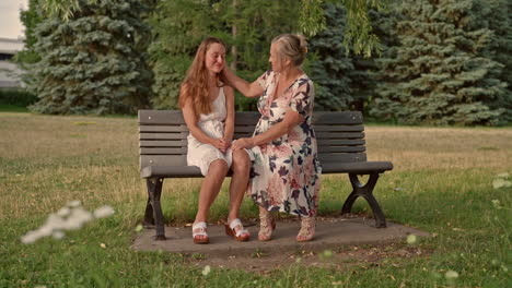 a mother warmly embraces her young adult daughter after an emotional conversation on a park bench, captured in a gentle dolly shot to the right under soft golden evening light