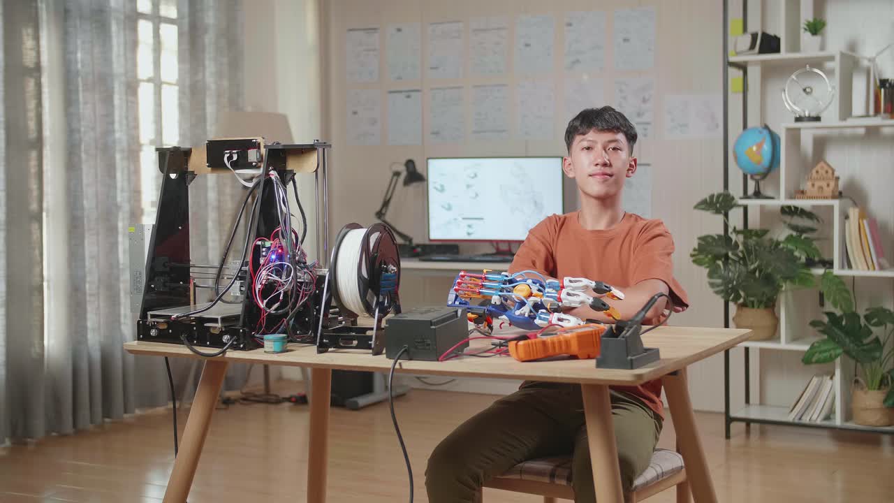 아시아 소년이 미소 짓고 집에서 사이보그 손에 대해 일하면서 카메라에 팔을 고 있습니다.