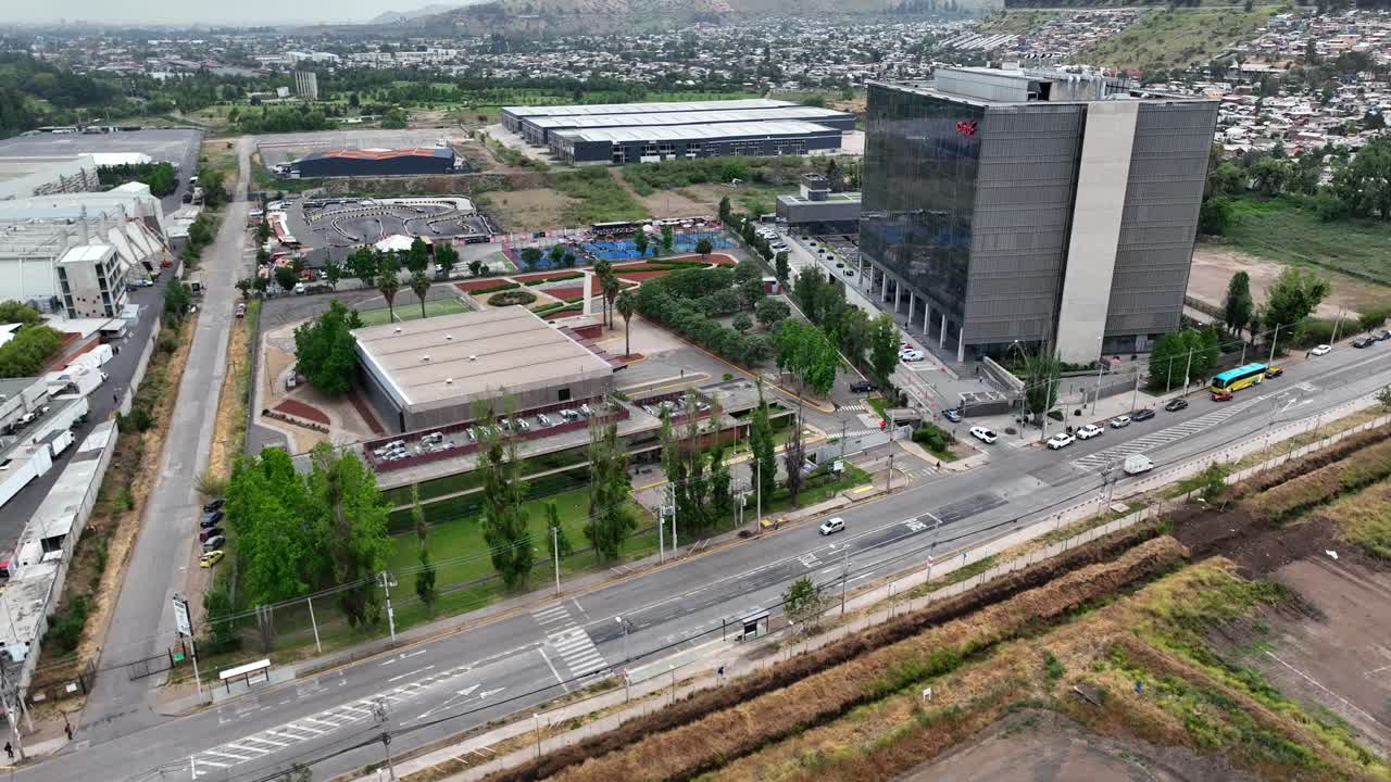Orbiting drone aerial of modern industrial park with commercial buildings, parking lots, highway intersection, and urban cityscape