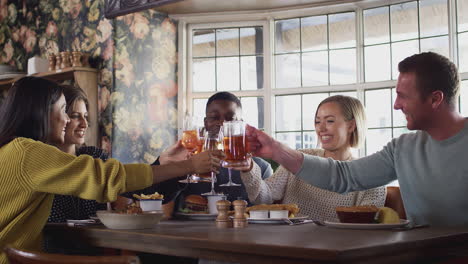 grupo de amigos haciendo un brindis mientras se reúnen para comer en un pub inglés tradicional