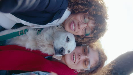 two happy girlfriends resting with dog in park and video calling