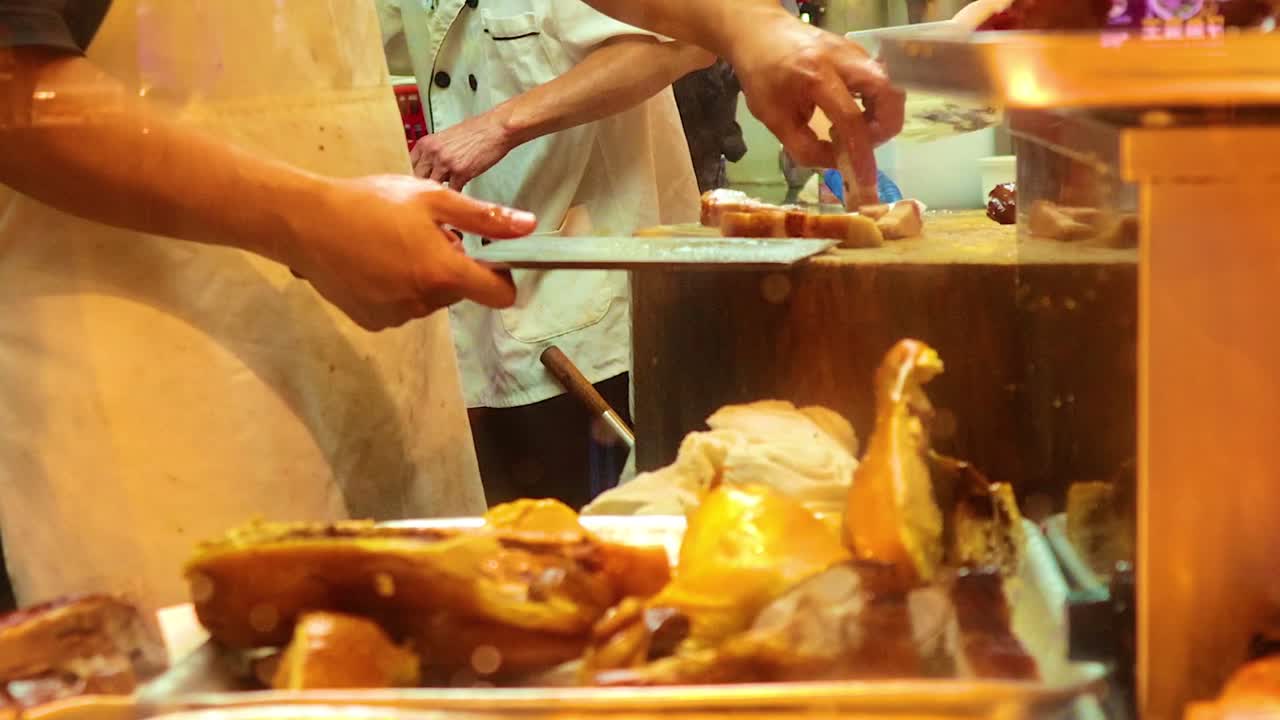 A chef expertly slices roast pork on a wooden block, showcasing precision and skill in a bustling kitchen.