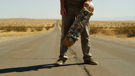 man holding skateboard on empty desert road