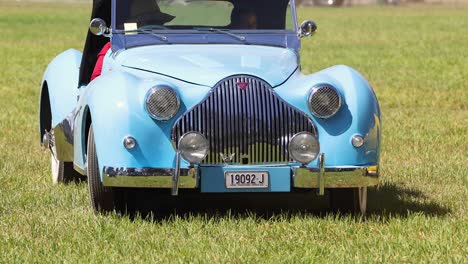 classic blue car driving across grass field.