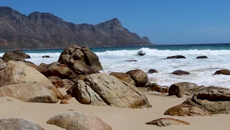 Waves-crashing-into-a-rocky-coastline-beach-with-mountain-range-in-the-background