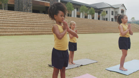 video de niñas diversas enfocadas practicando yoga en esteras frente a la escuela