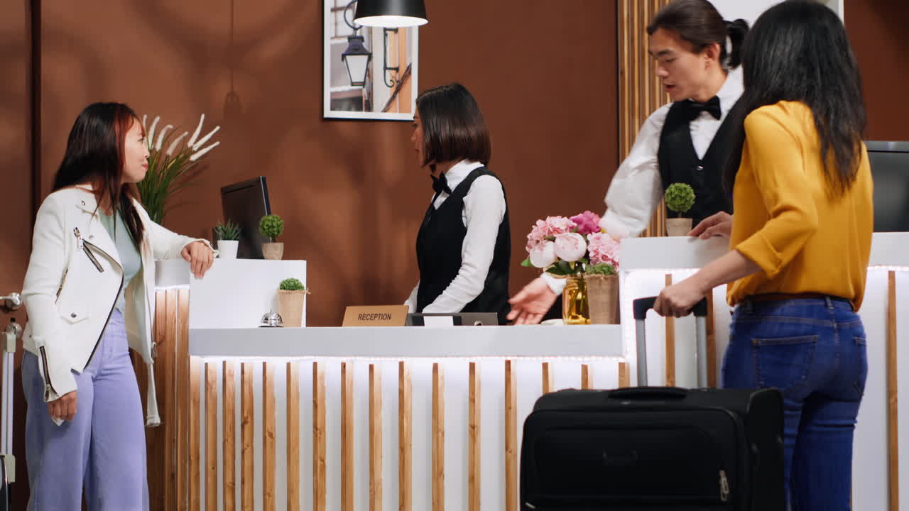 아시아 여자 들 이 로비 에 있는 리셉션 데스크 에서 리셉션 담당자 와 대화 하고 있다