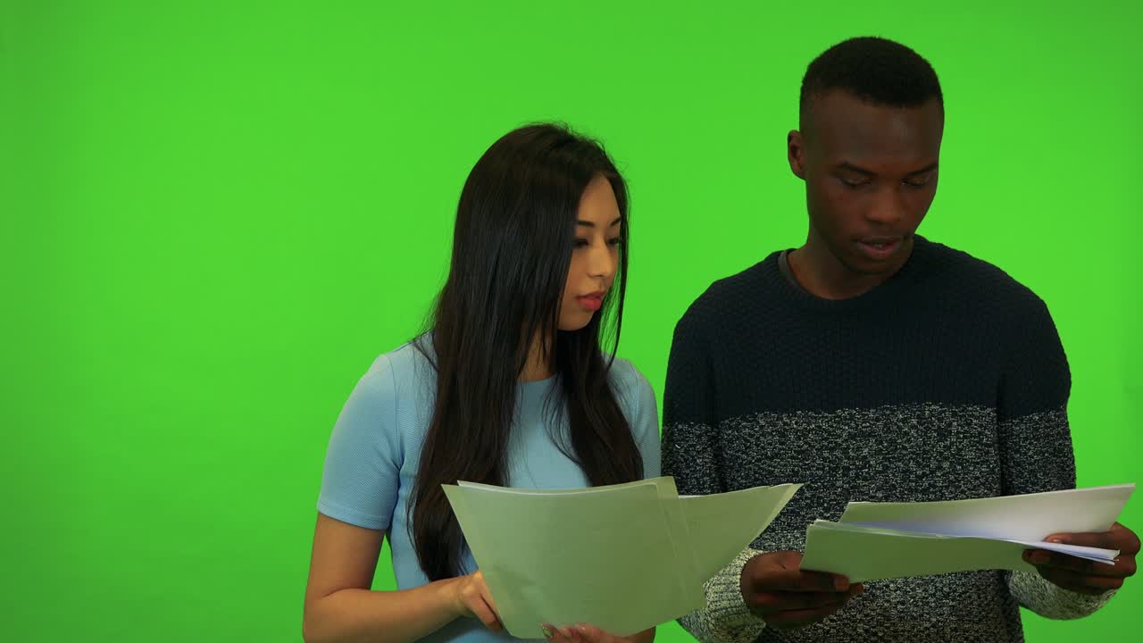 una joven asiática y un joven negro sostienen papeles, ella le explica algo - estudio de pantalla verde